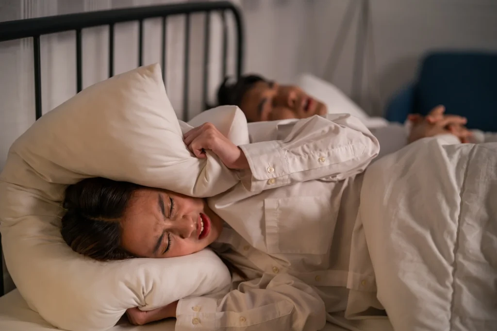 Asian woman feel frustrated from husband snoring while sleep at night.